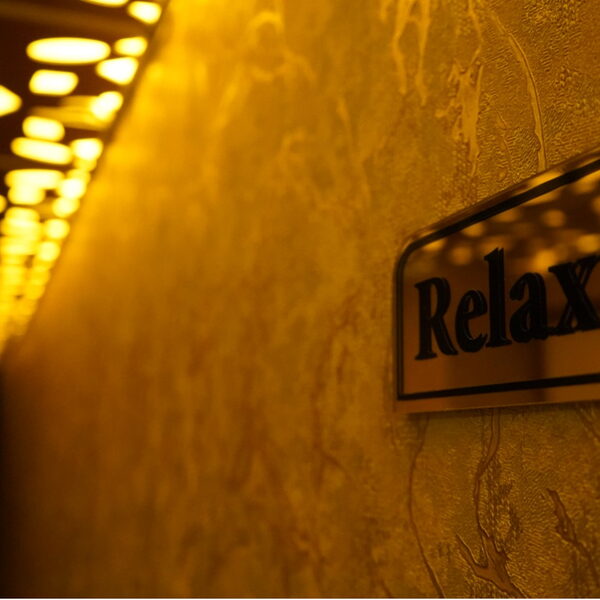 لقطة مقربة للافتة Relax النحاسية على جدار رخامي مع أضواء سقف غير واضحة في الخلفية